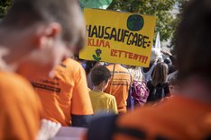 Ein junger Teilnehmer einer Klimademo hält ein Plakat mit der Aufschrift "Hausaufgabe: Klima retten!!!"