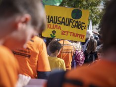 Ein junger Teilnehmer einer Klimademo hält ein Plakat mit der Aufschrift "Hausaufgabe: Klima retten!!!"