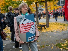 Eine Frau hält auf einer Demo ein Plakat von Die Linke mit der Aufschrift "Menschen entlasten. Preise deckeln. Übergewinne besteuern."