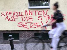 Eine Fahrradfahrerin fährt an einer Wand mit dem Graffiti "Spekulanten auf die Straße setzen" vorbei.
