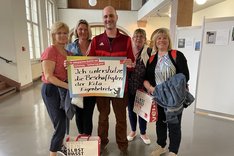 Vier Erzieherinnen vom Kita-Eigenbetrieb Süd-Ost mit Georg Frankl von der Linksfraktion im Foyer des Rathaus Neuköllns. Frankl hält ein Schild mit der Aufschrift "Ich unterstütze die Beschäftigten der Kita-Eigenbetriebe"