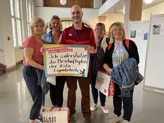 Vier Erzieherinnen vom Kita-Eigenbetrieb Süd-Ost mit Georg Frankl von der Linksfraktion im Foyer des Rathaus Neuköllns. Frankl hält ein Schild mit der Aufschrift "Ich unterstütze die Beschäftigten der Kita-Eigenbetriebe"