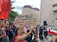 Eine Teilnehmerin der Kundgebung von DIE LINKE. Neukölln gegen die Kürzungsmaßnahmen am 5. Juli 2023 hält ein Schild mit der Aufschrift: "2,8 Millionen Kinder und Jugendliche wachsen in Deutschland in Armut auf. 53 Milliarden Euro private Gewinnanteile schütten 40 Dax-Konzerne an ihre Aktionär*innen aus!"