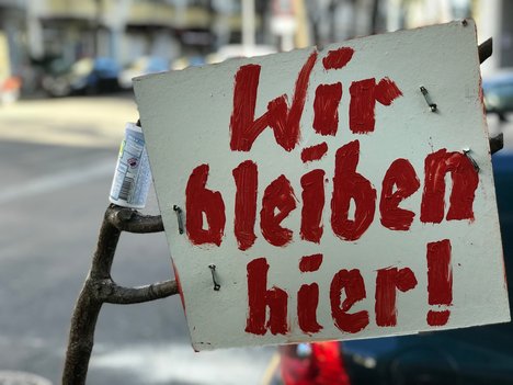 Plakat mit der Aufschrift "Wir bleiben hier!"