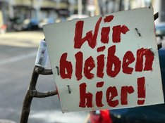Plakat mit der Aufschrift "Wir bleiben hier!"